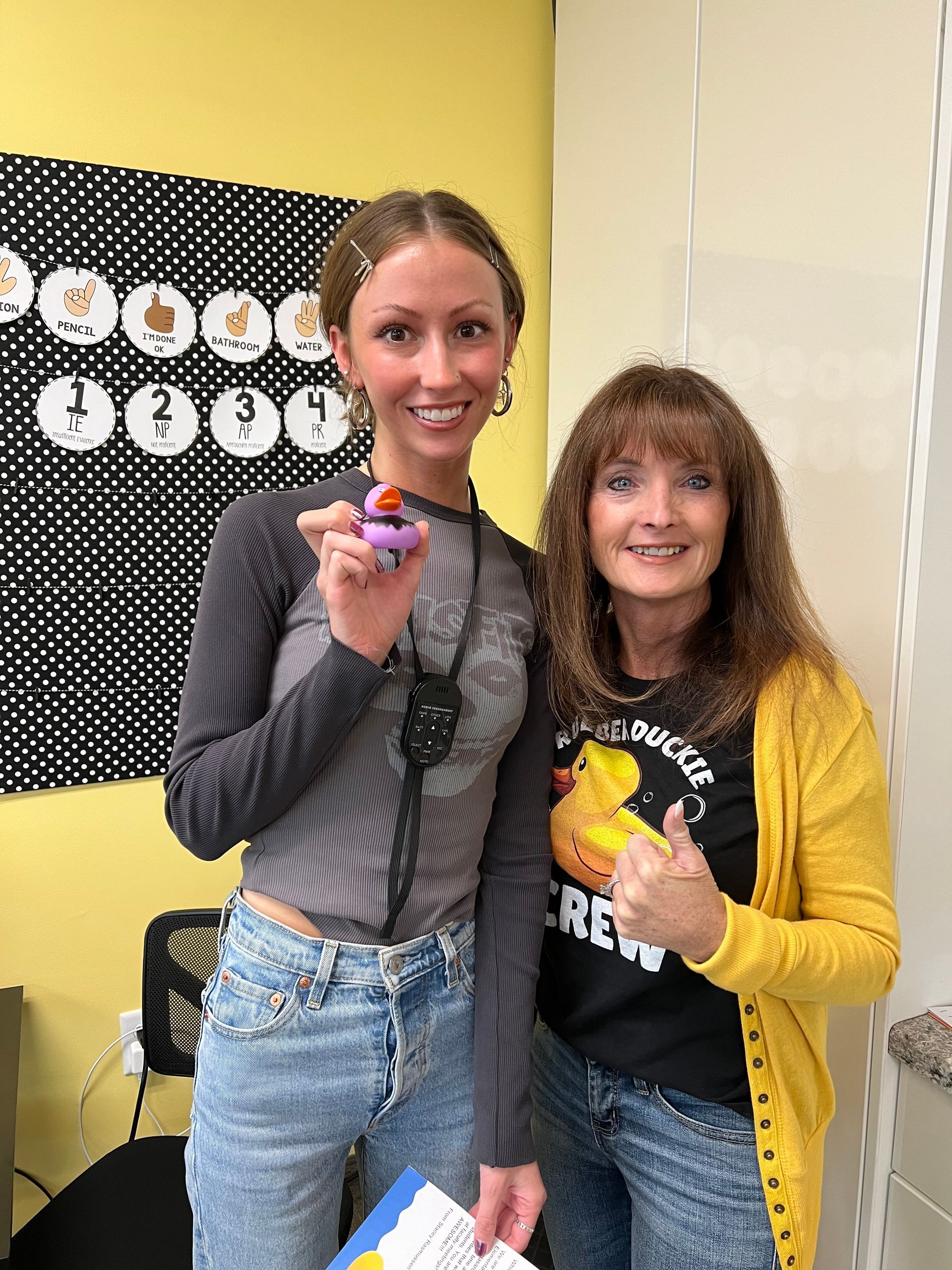 Two women are standing next to each other in a room holding cupcakes.