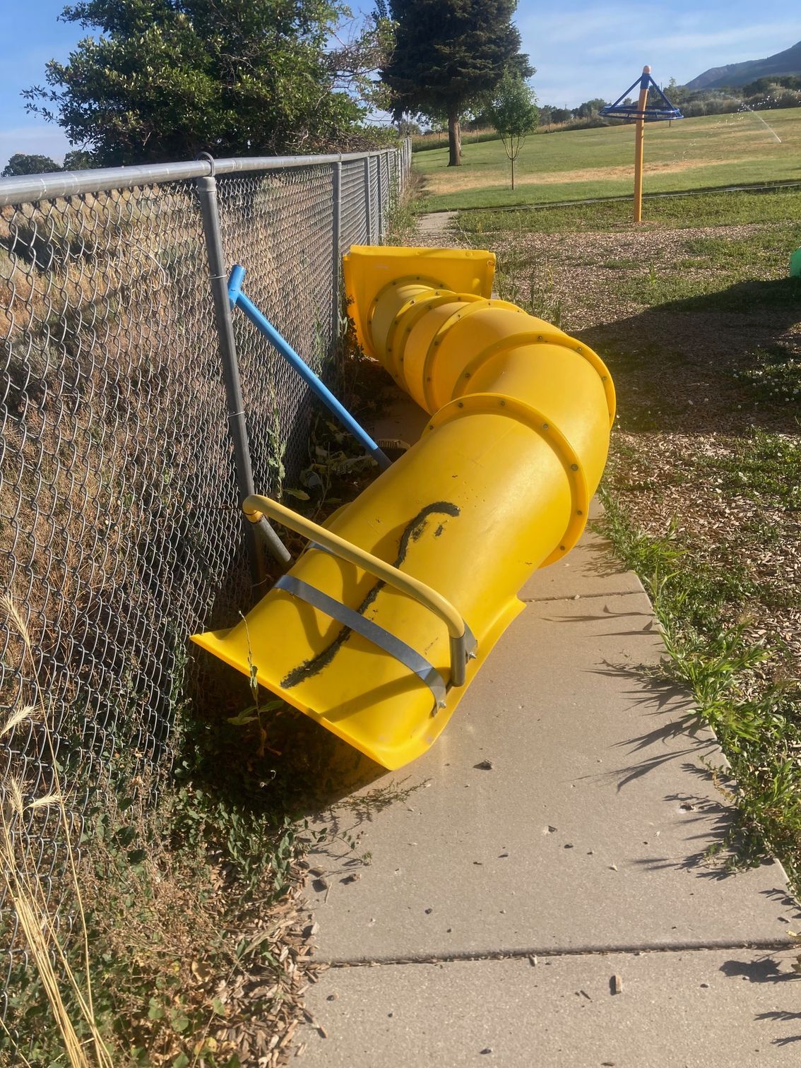 A yellow slide is sitting on the sidewalk next to a chain link fence