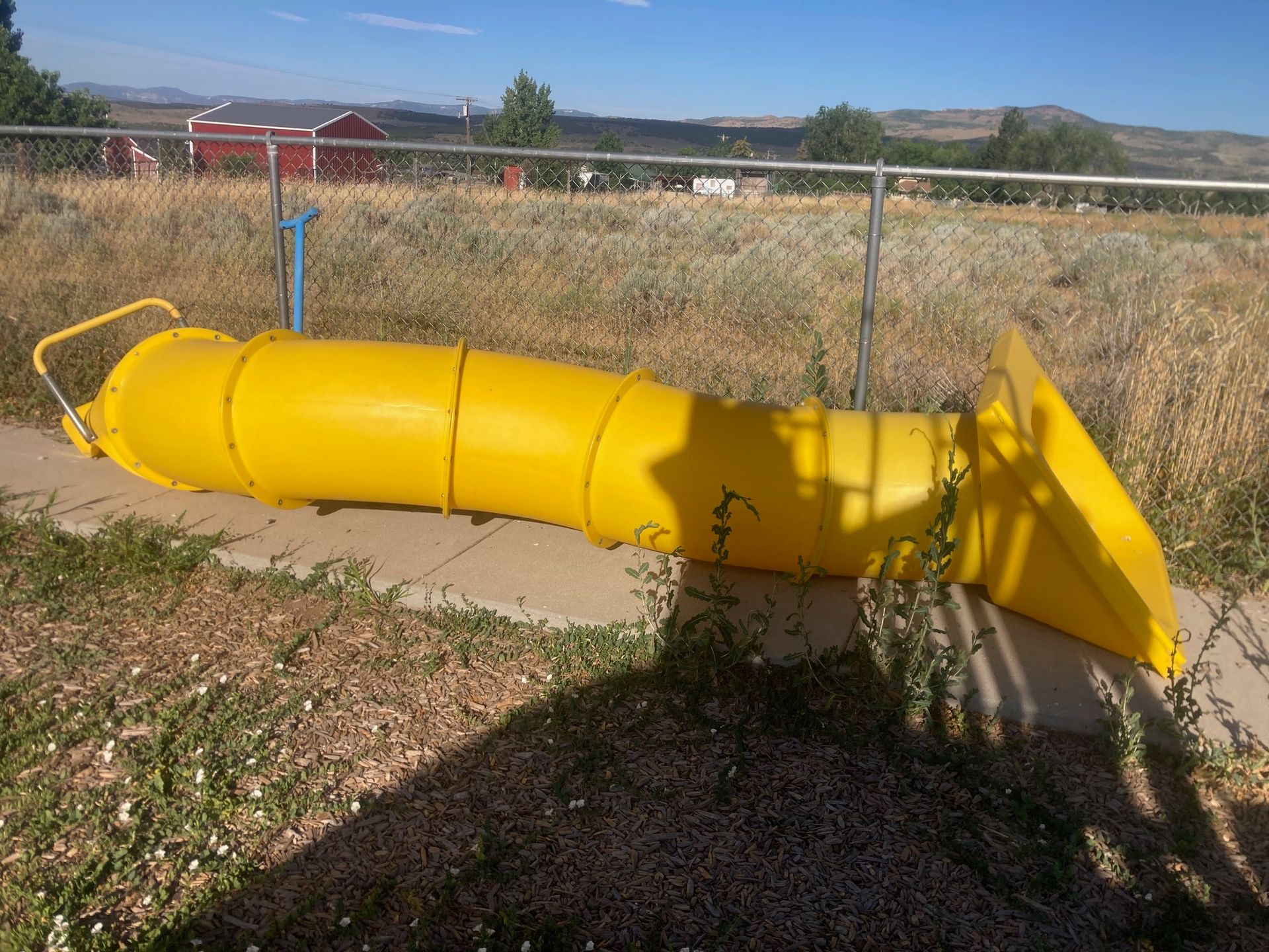 A yellow slide is sitting on the ground next to a fence.