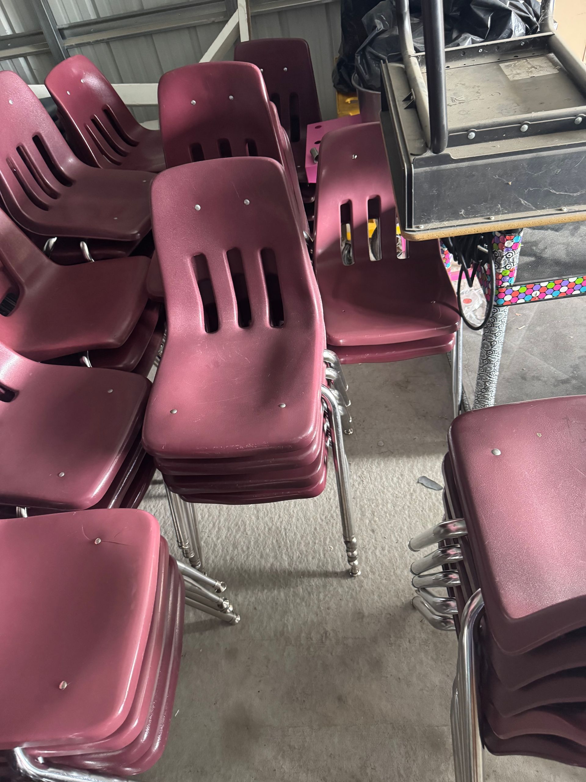 A stack of maroon-colored school chairs with chrome legs sit inside.