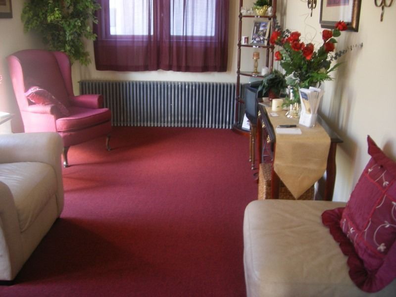 Cozy room with red carpet, burgundy accent chair, cream sofa, and a table with red roses.