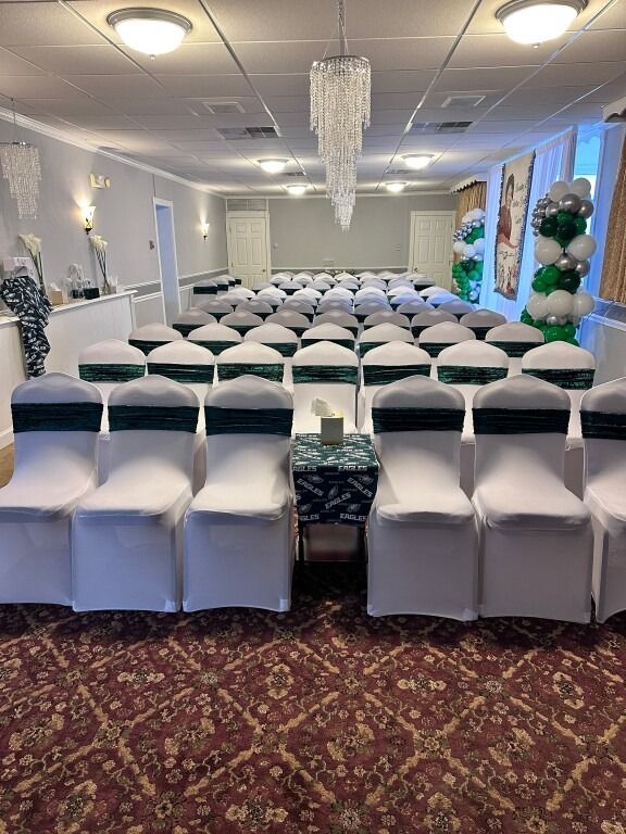 Rows of white chairs with green sashes set up in a room with a chandelier; for a ceremony.