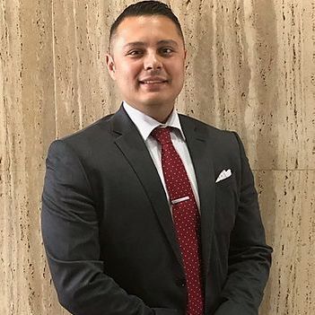A man in a suit and tie is standing in front of a wall.