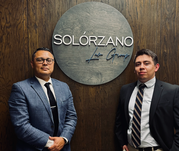 Two men in suits and ties are standing in front of a solorzano sign.