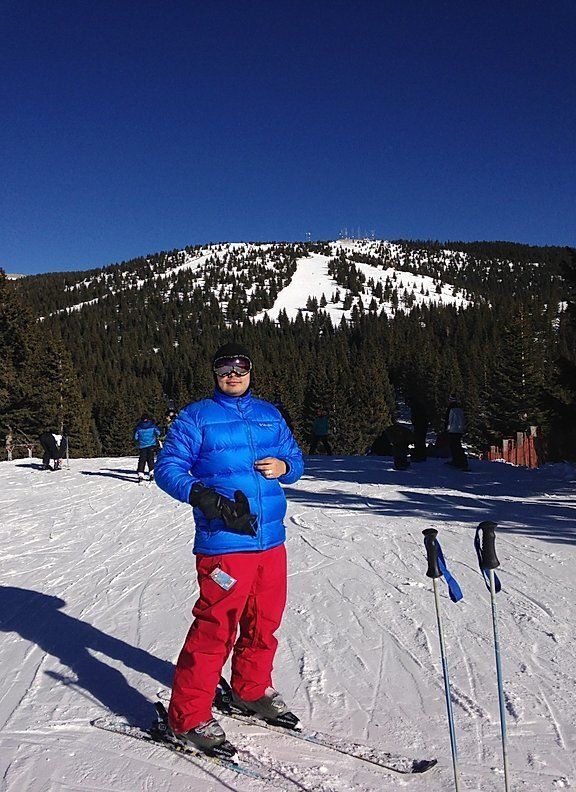 A man in a blue jacket and red pants is standing on skis on a snowy slope.