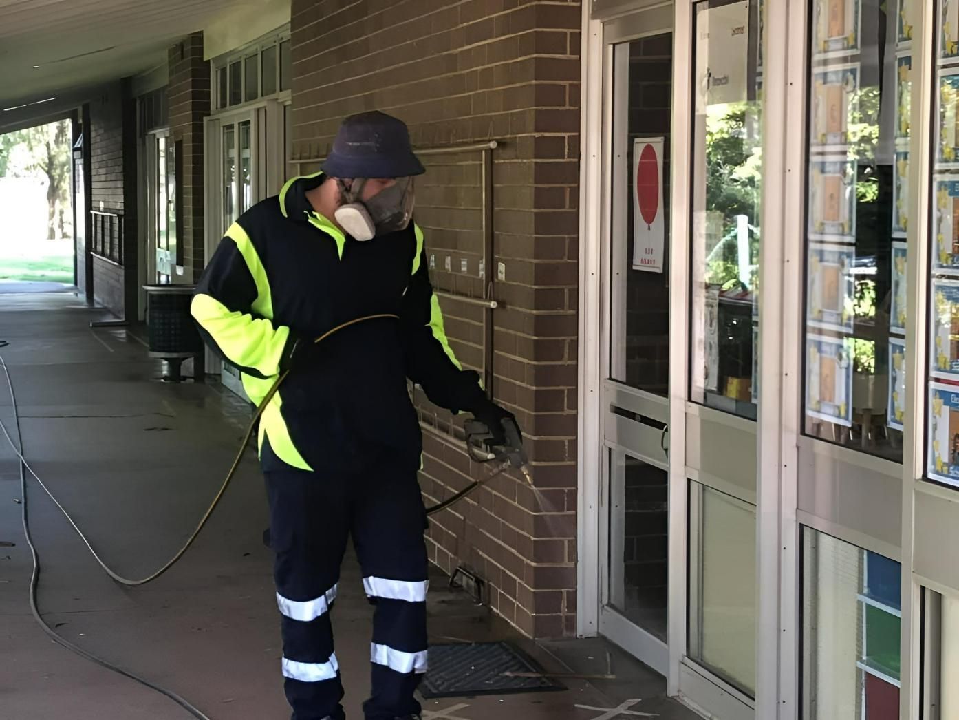 A Man is Spraying a Commercial Building With a Hose — TC Pest & Termite Control In Mittagong, NSW