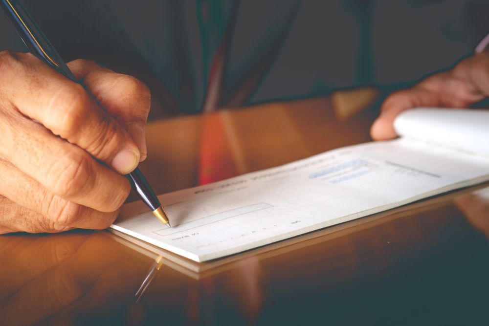 A person is writing a check with a pen on a table.