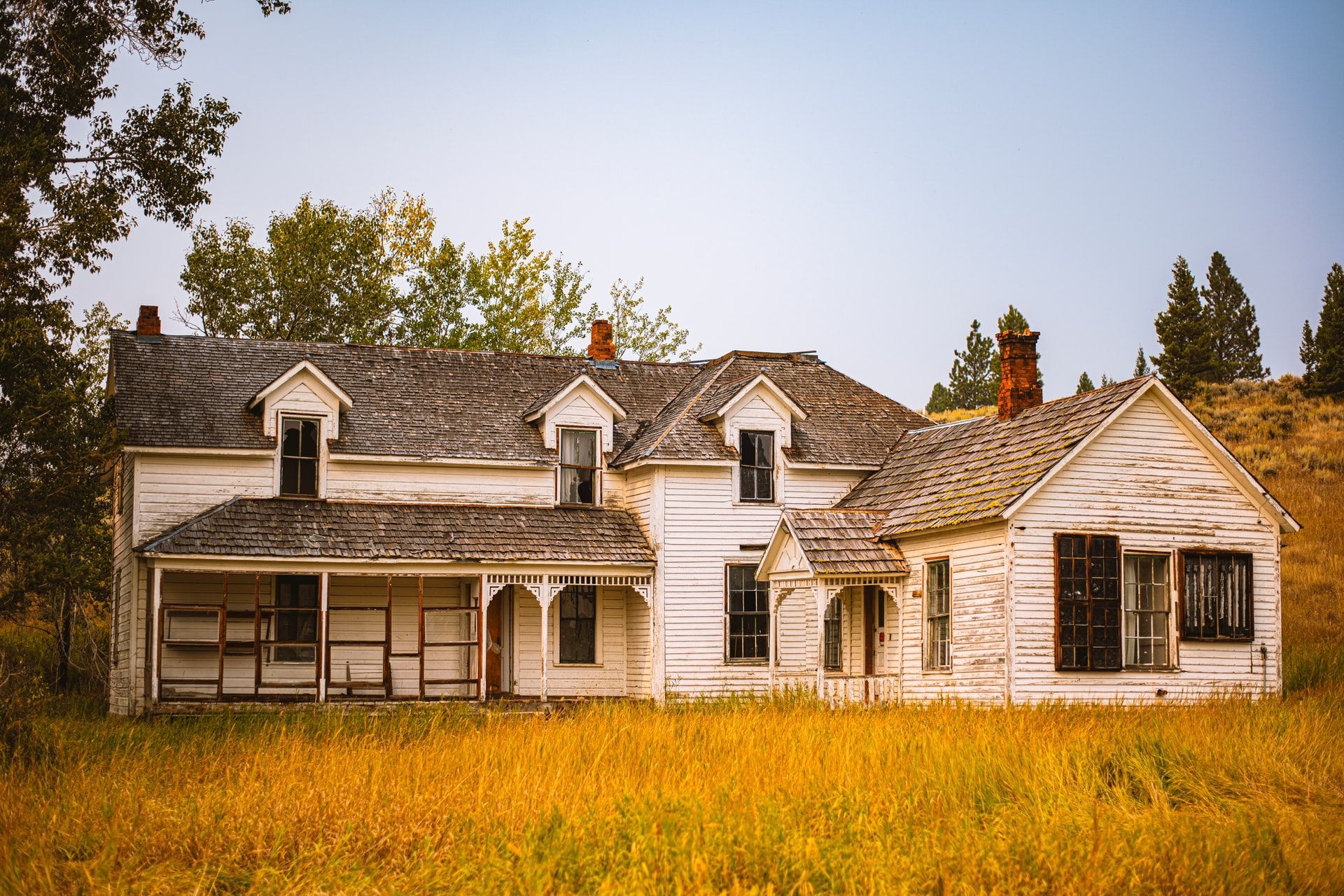 An old white house is sitting in the middle of a field.