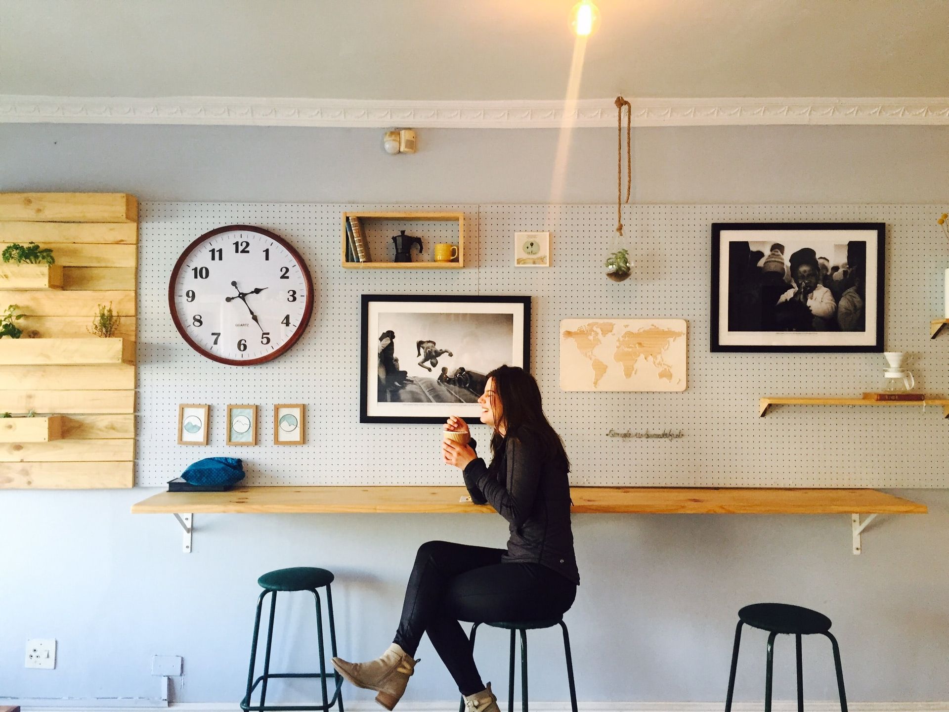 A woman is sitting on a stool in front of a wall with a clock on it