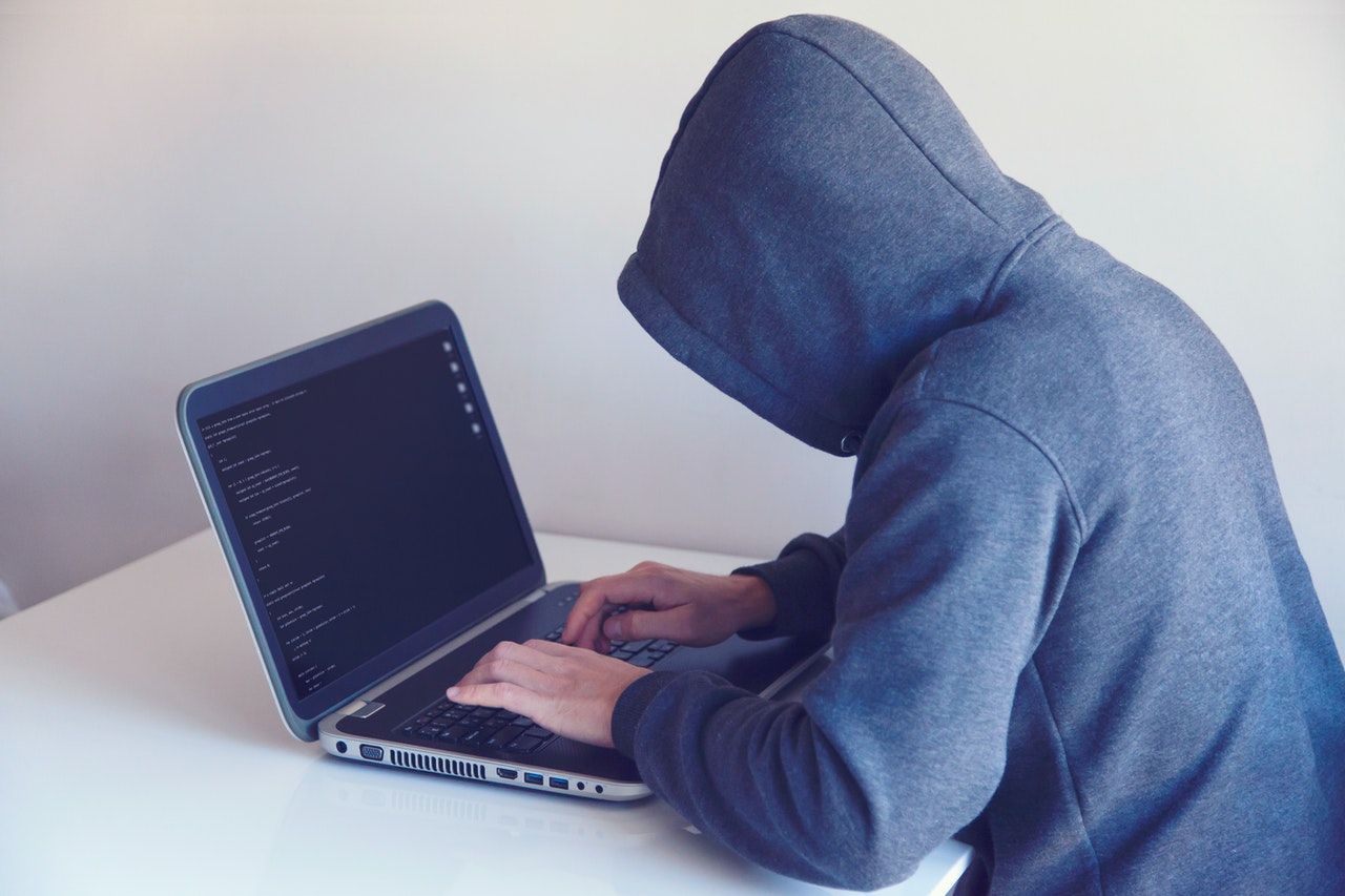 A man in a hoodie is typing on a laptop computer.