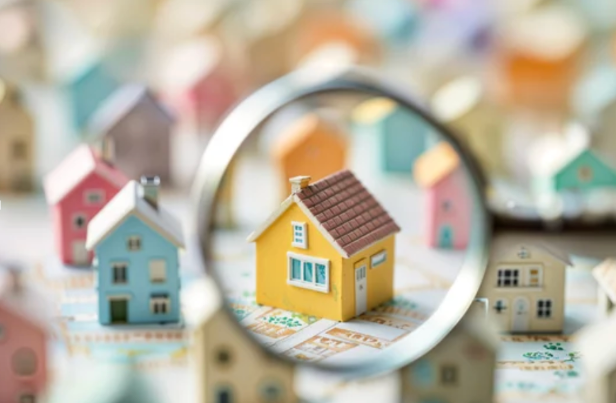 Magnifying glass focusing on a small yellow house among a group of miniature homes.