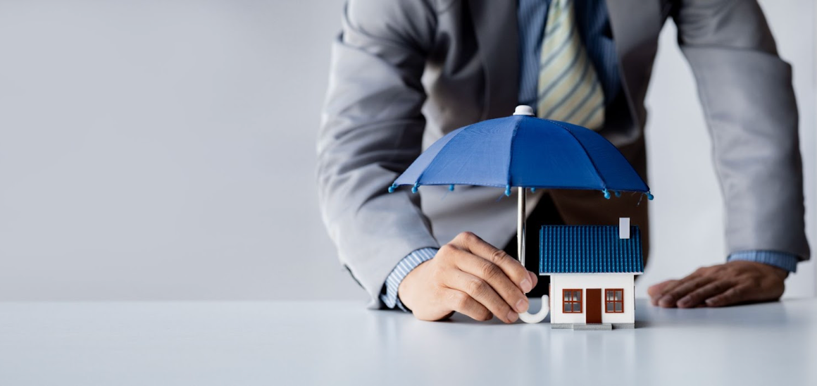 Hand holding an umbrella over a small model home, representing title insurance protection and home s