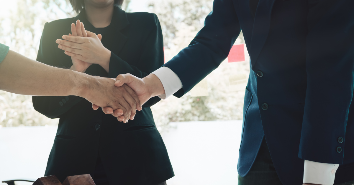 Business professionals shaking hands over real estate closing documents with house keys and a model