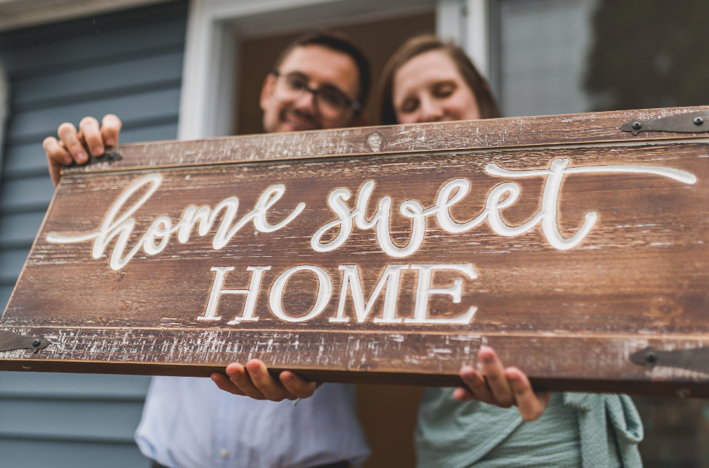 A man and a woman are holding a wooden sign that says home sweet home.