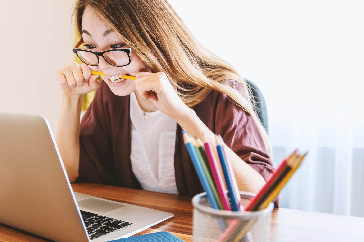 A woman is biting a pencil while looking at a laptop computer.