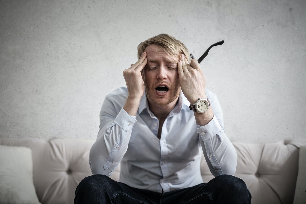 A man is sitting on a couch with his hands on his head.