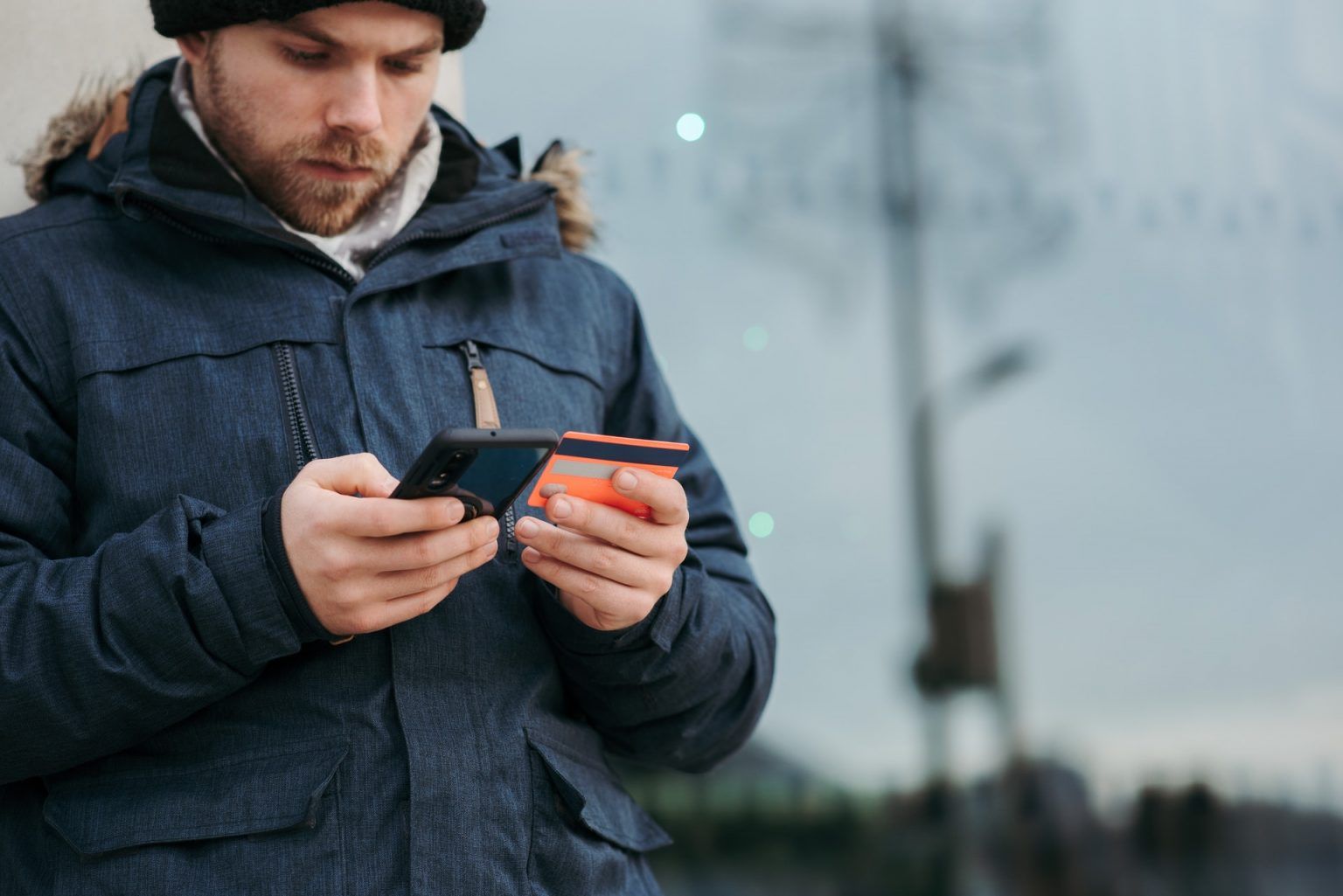 A man is holding a credit card and a cell phone.