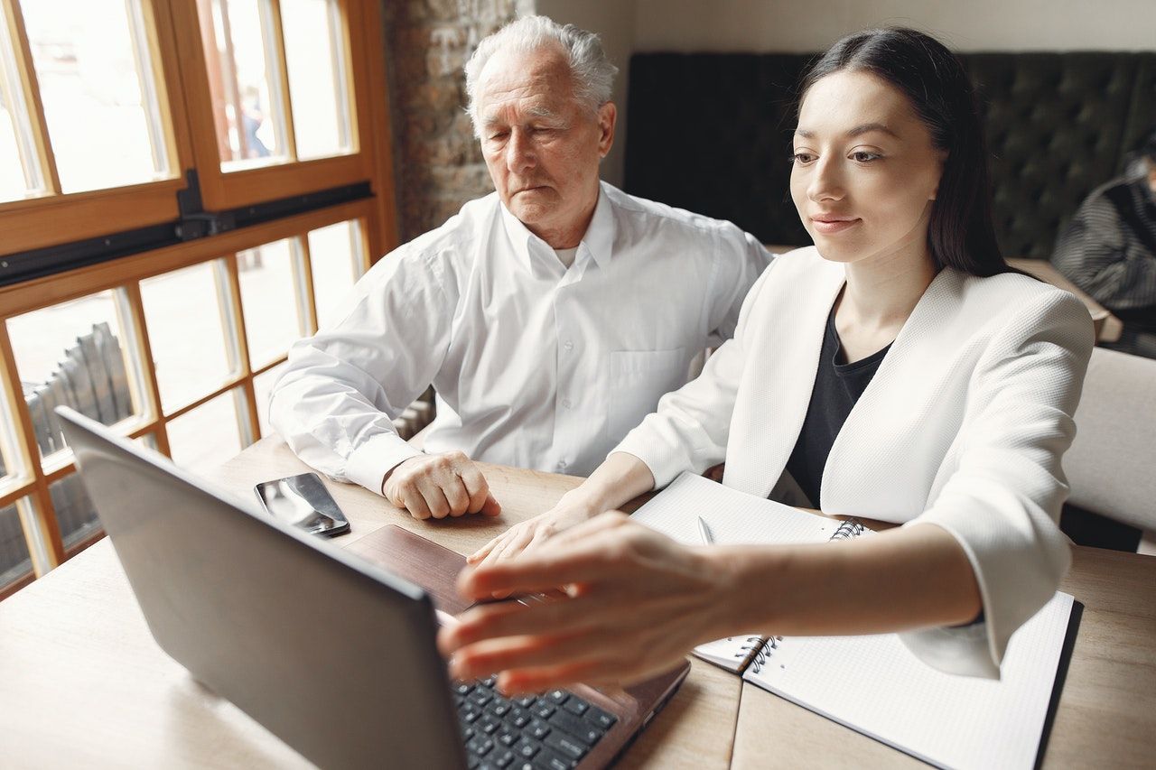 A man and a woman are sitting at a table looking at a laptop computer.