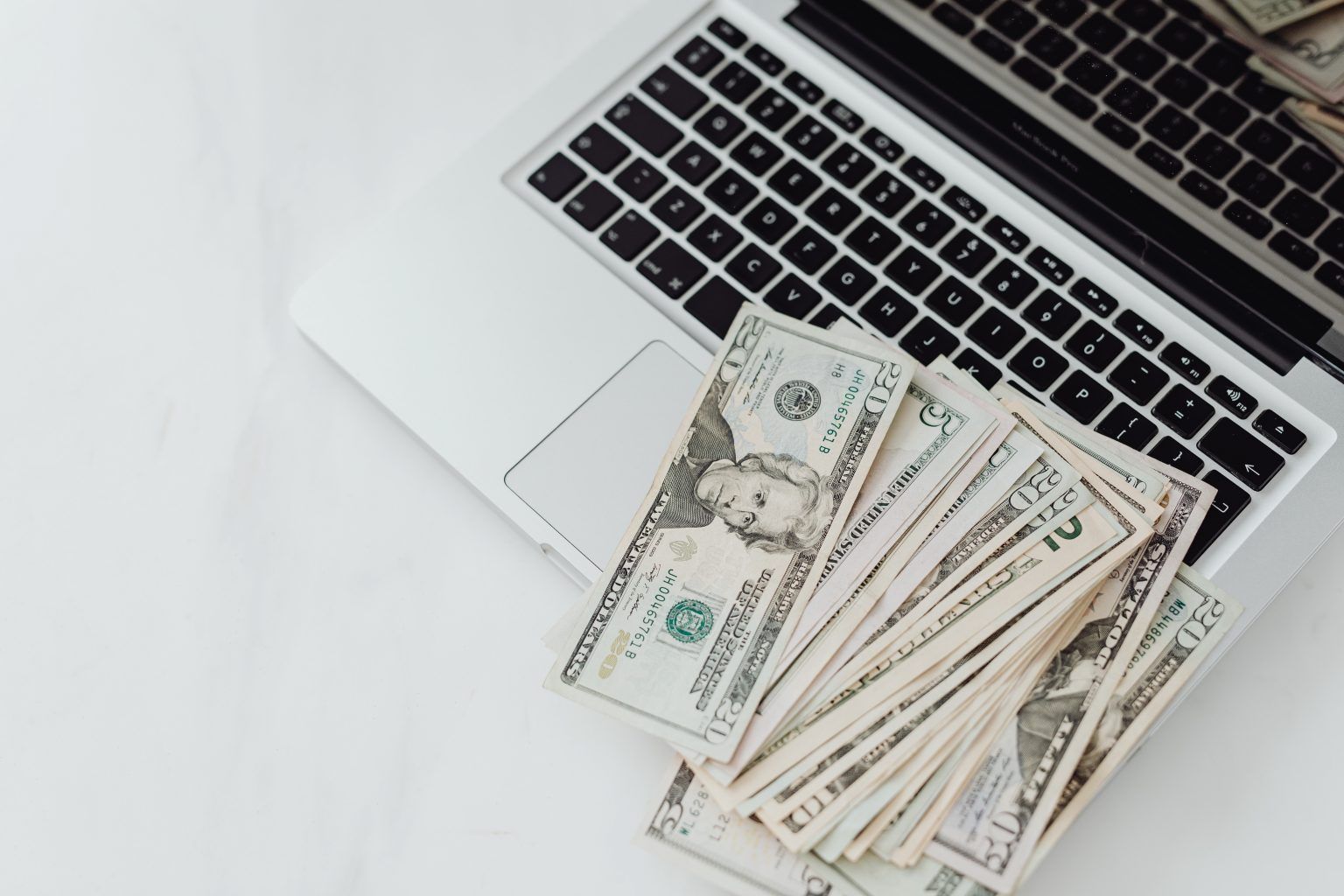 A pile of money is sitting on top of a laptop keyboard.