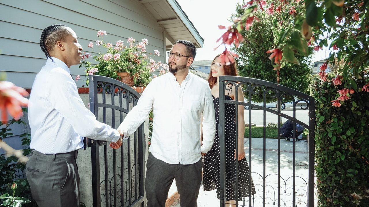 A man and woman are shaking hands with a real estate agent in front of a house.