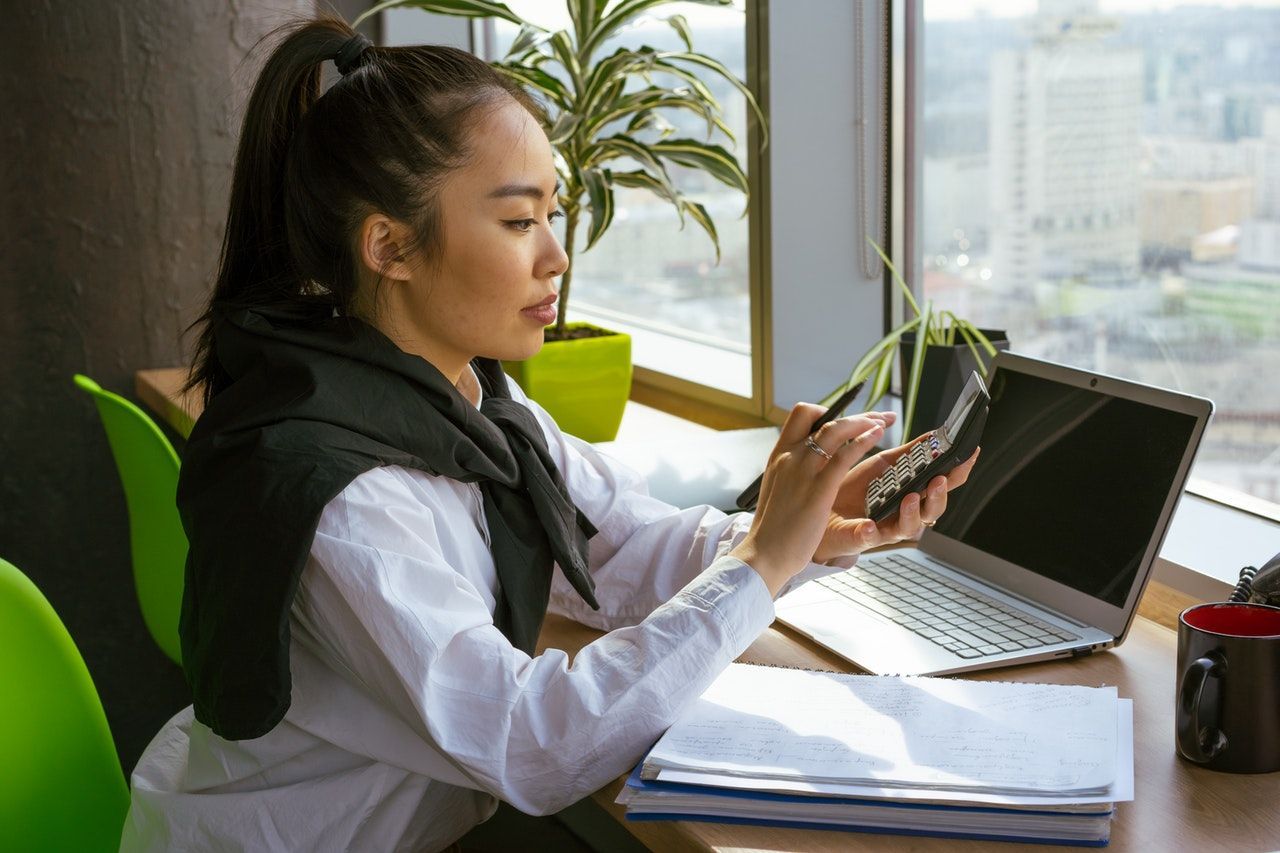 A woman is sitting at a desk with a laptop and a cell phone.