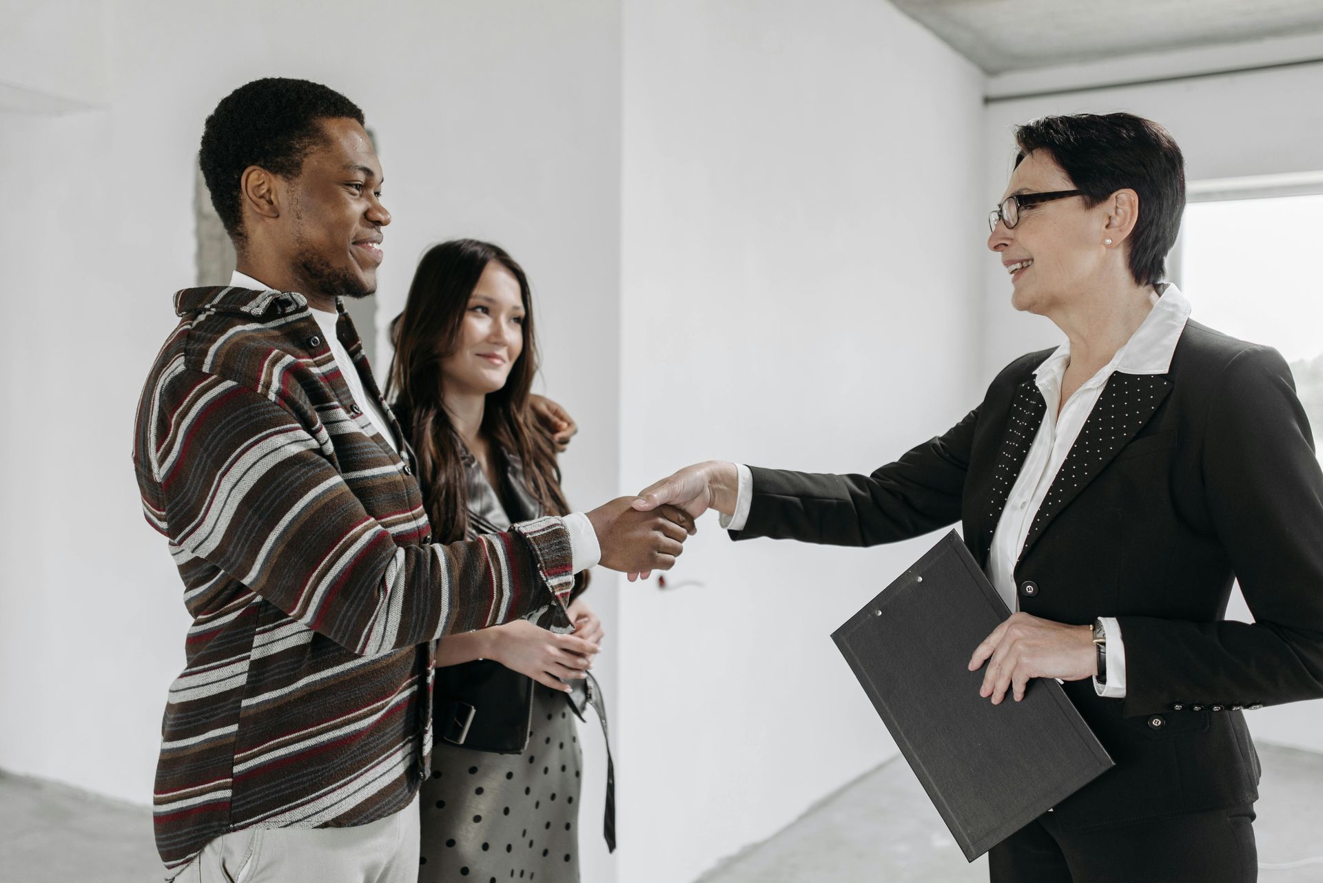 A man and woman are shaking hands with a real estate agent in an empty room.