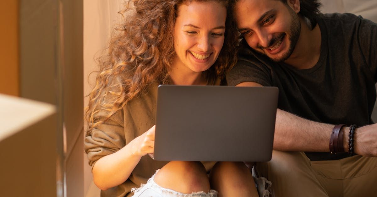 A man and a woman are sitting on a couch looking at a laptop computer.