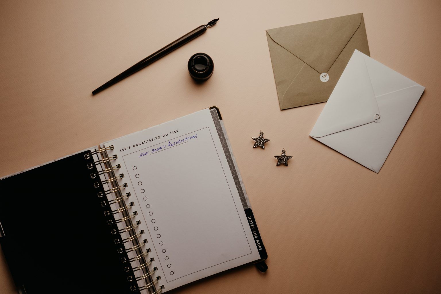 A notebook , pen , envelope , and earrings are on a table.