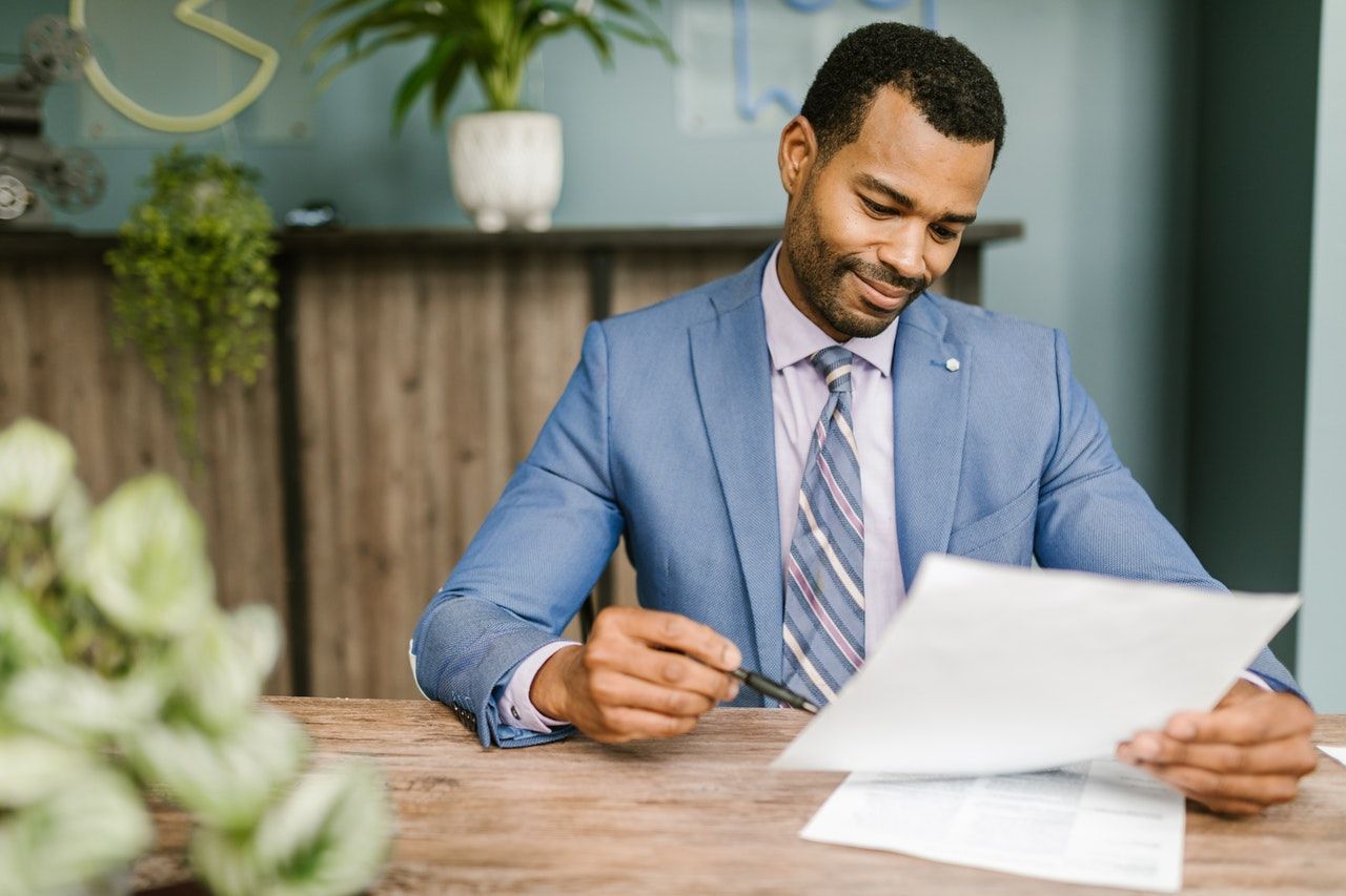 A man in a suit and tie is sitting at a table reading a piece of paper.