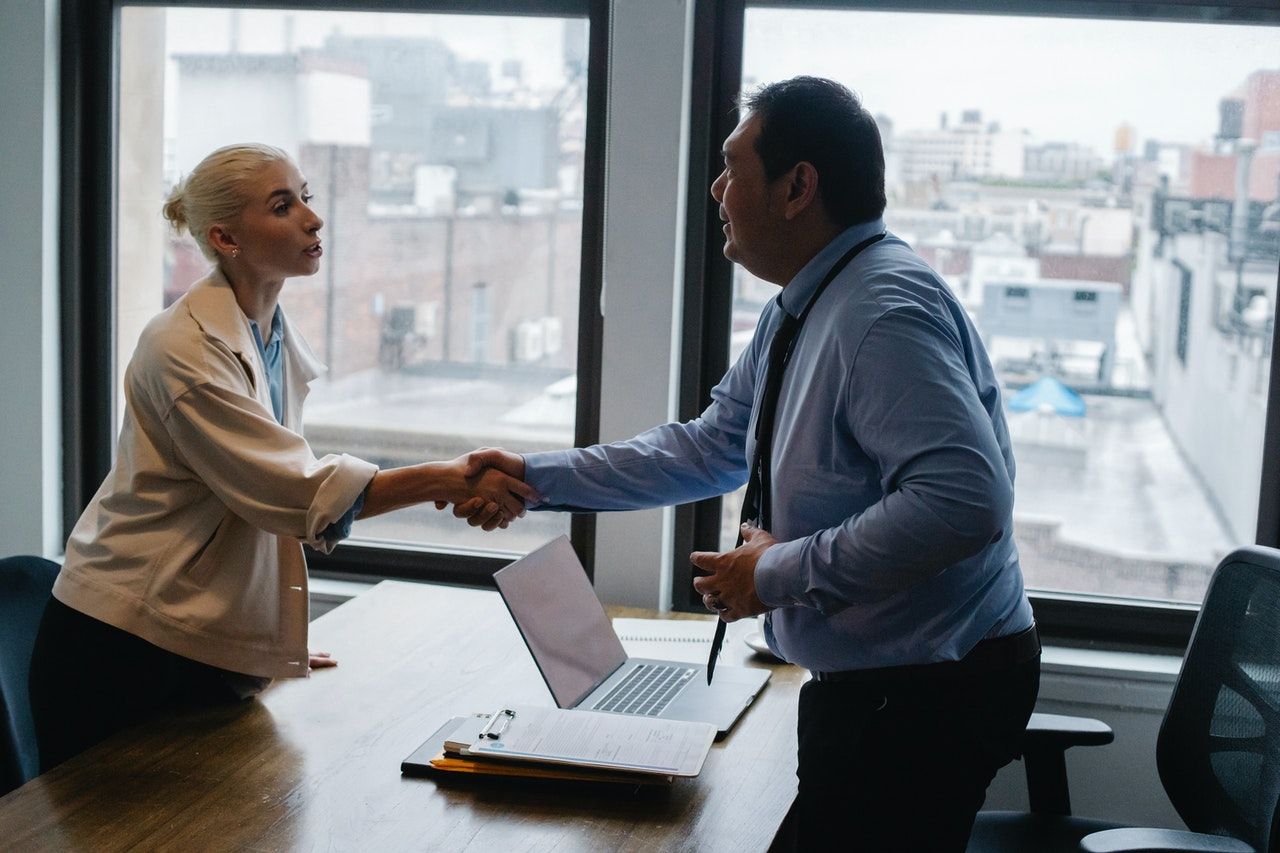 A man and a woman are shaking hands while sitting at a table with a laptop.