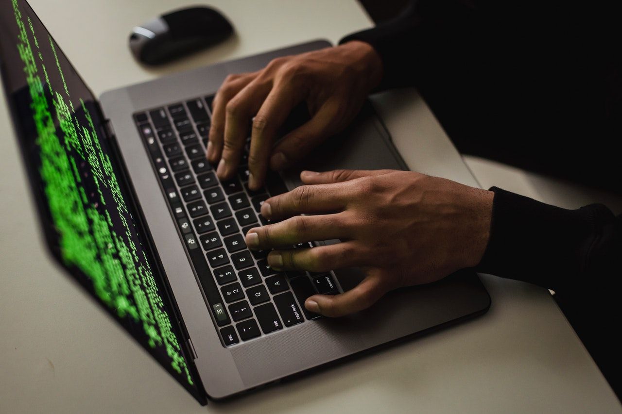 A person is typing on a laptop computer with a green screen.