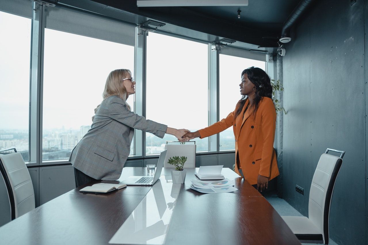 Two women are shaking hands in a conference room.