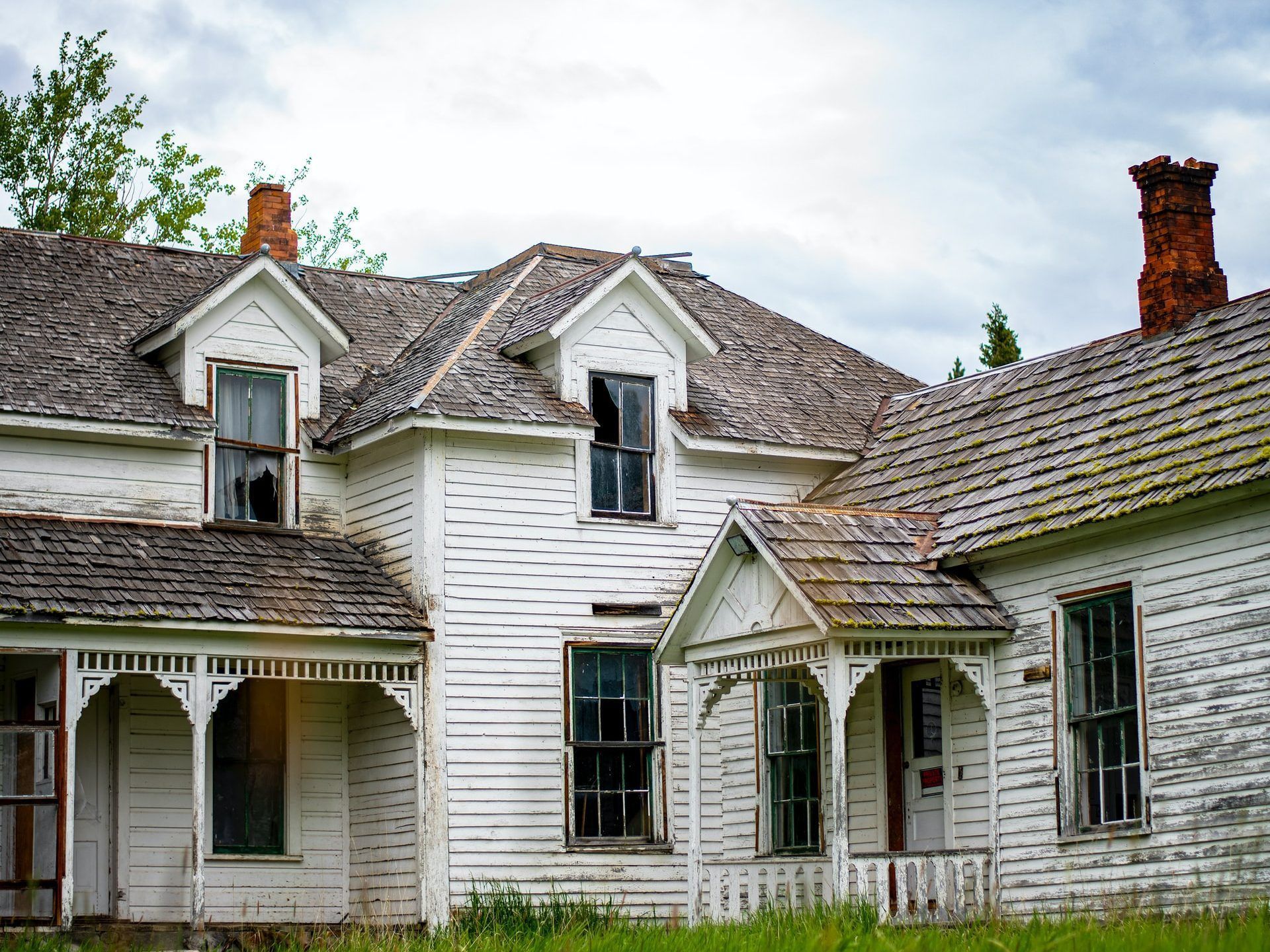 An old white house with a broken window and a chimney.