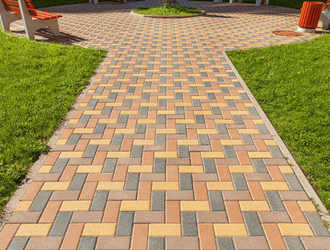 A nice brick-paved walkway in a yard with a bench in the background