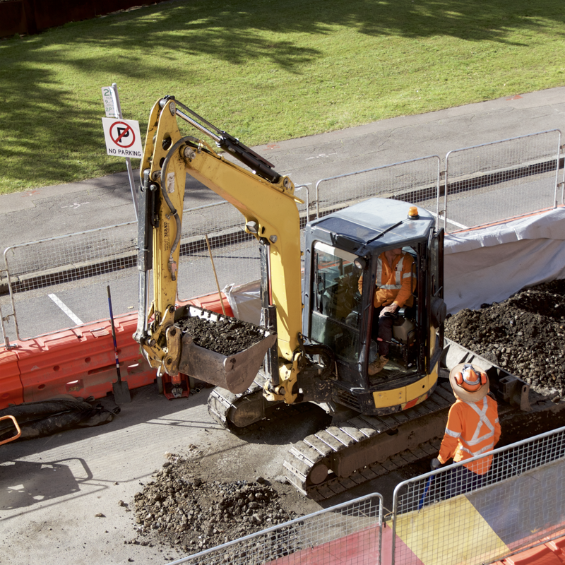 a yellow excavator is digging a hole on the side of the road .