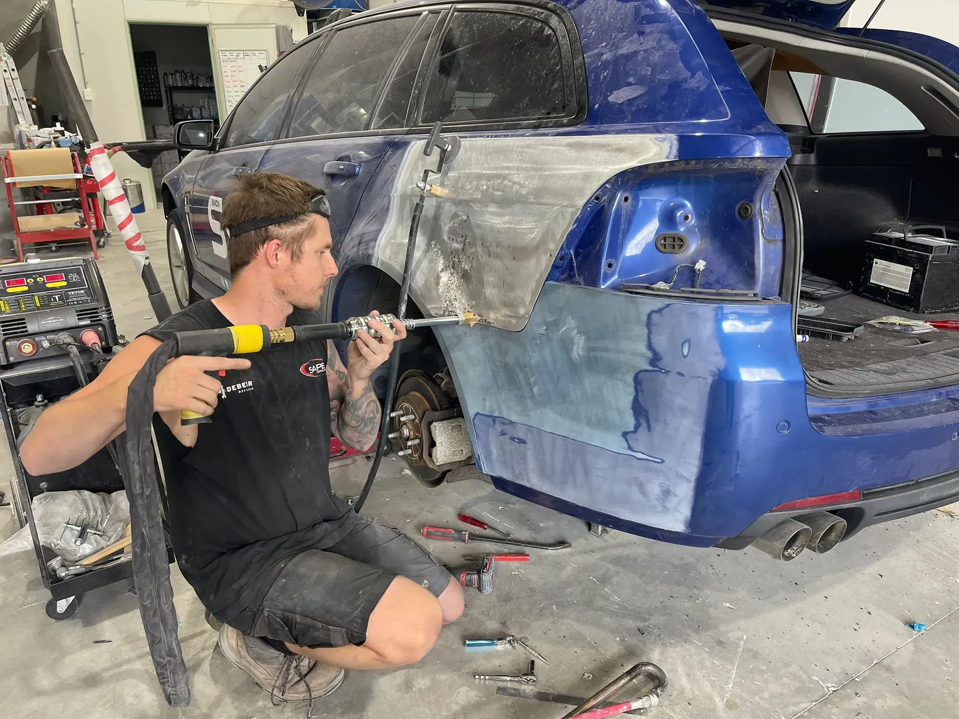 Man using a tool to work on the rear panel of a blue car in a repair shop. — Coolum Smash Repairs in Coolum Beach, QLD