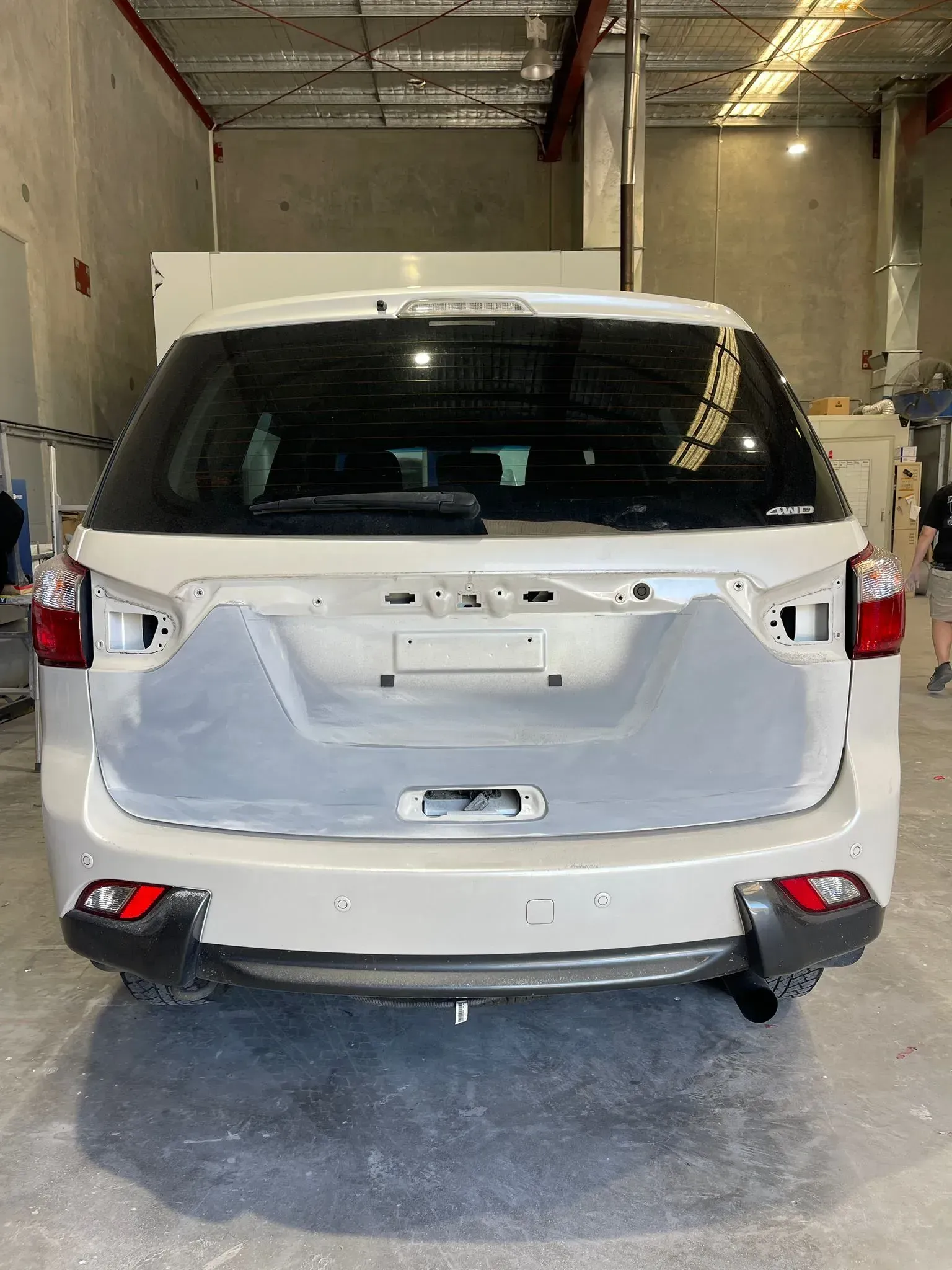 Rear view of a white SUV in a workshop. The bumper is prepared for paint with visible primer. — Coolum Smash Repairs in Coolum Beach, QLD
