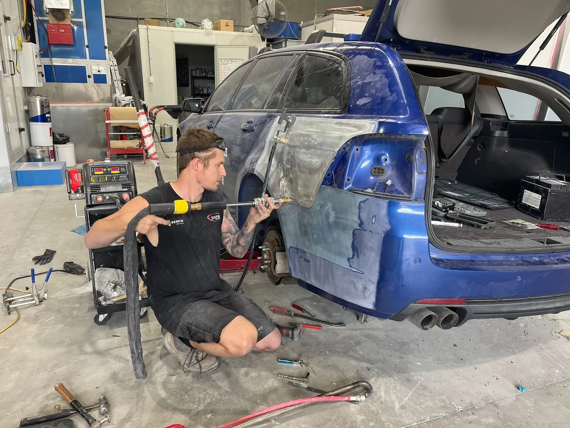 Mechanic repairing a blue car in a garage, using a tool on the body panel. — Coolum Smash Repairs in Coolum Beach, QLD