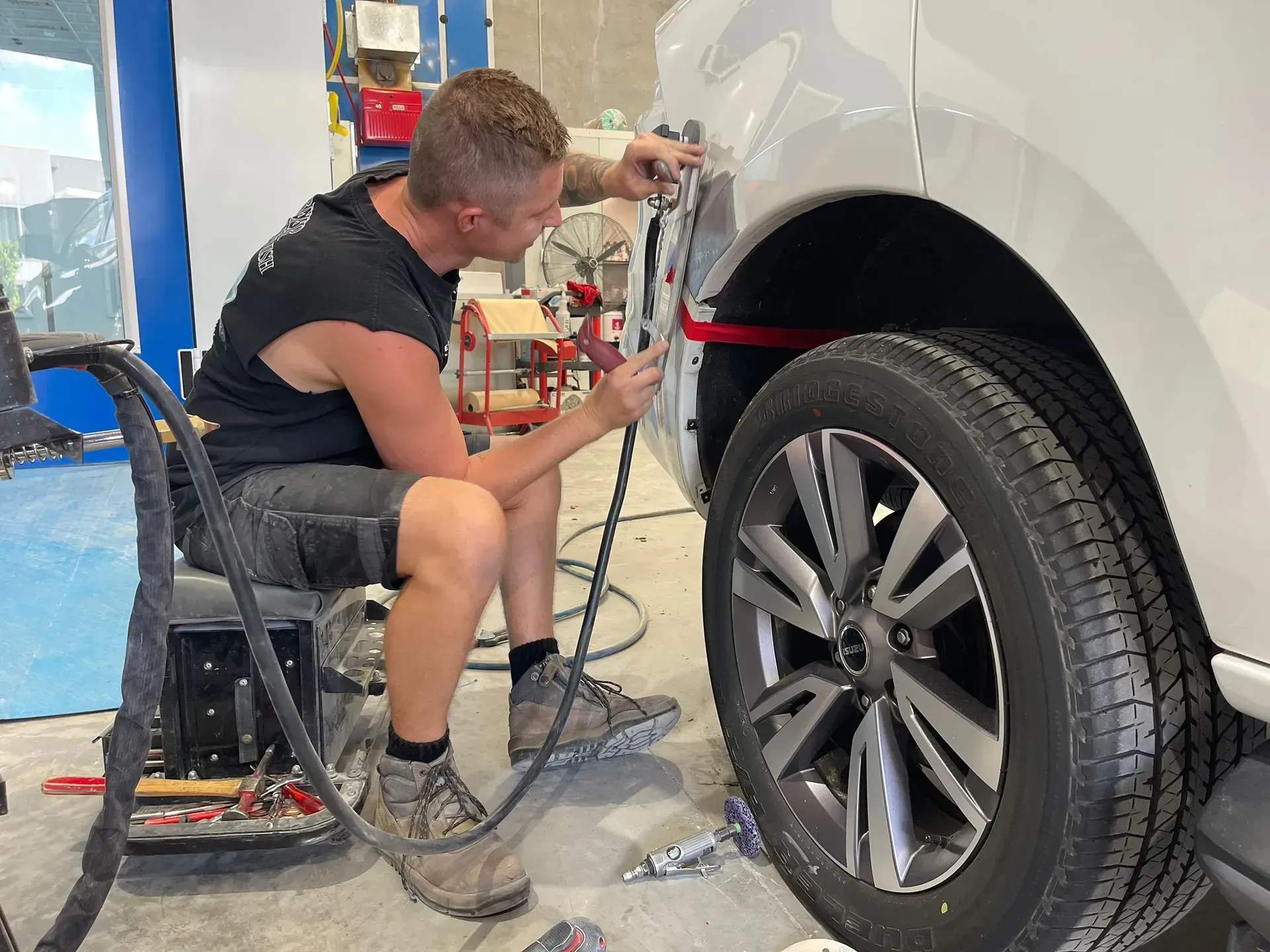 A mechanic repairs a dented white car fender using tools in a shop. — Coolum Smash Repairs in Coolum Beach, QLD