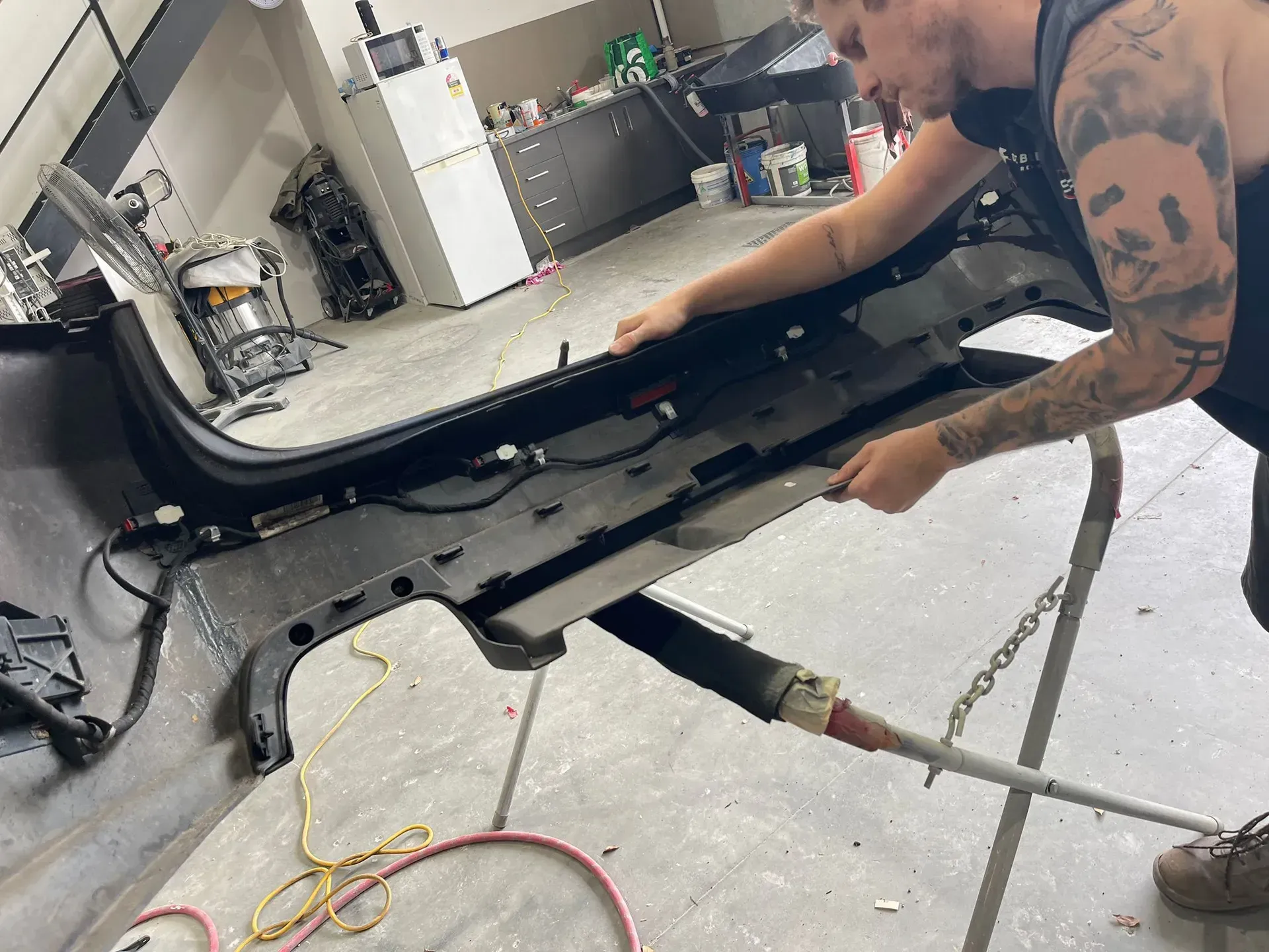 A person working on a car bumper in a workshop, using a tool. — Coolum Smash Repairs in Coolum Beach, QLD