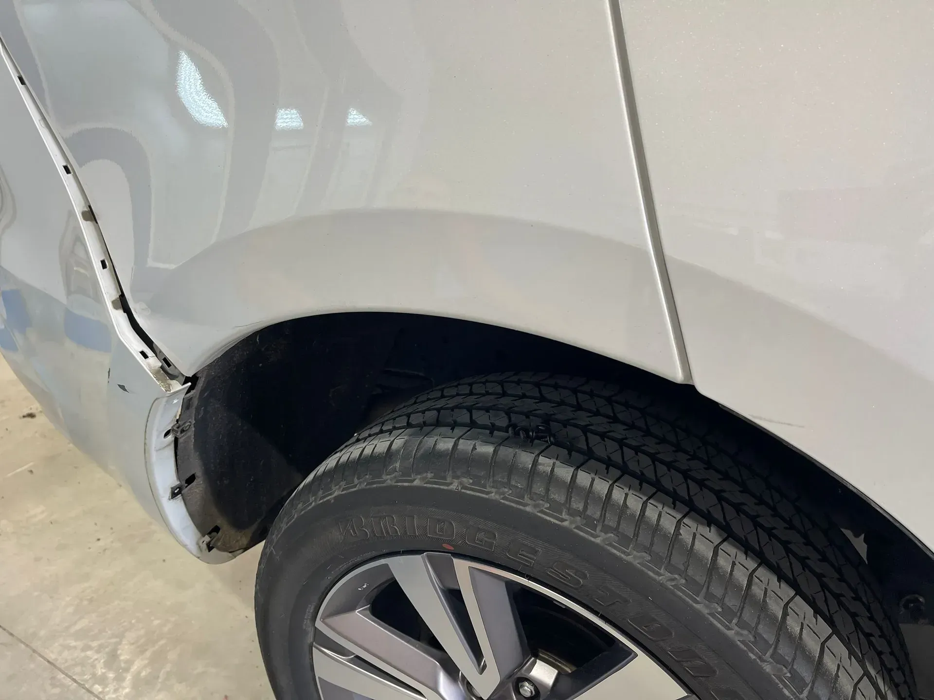 Damaged white car's rear quarter panel, dented above the tire and along door frame. — Coolum Smash Repairs in Coolum Beach, QLD