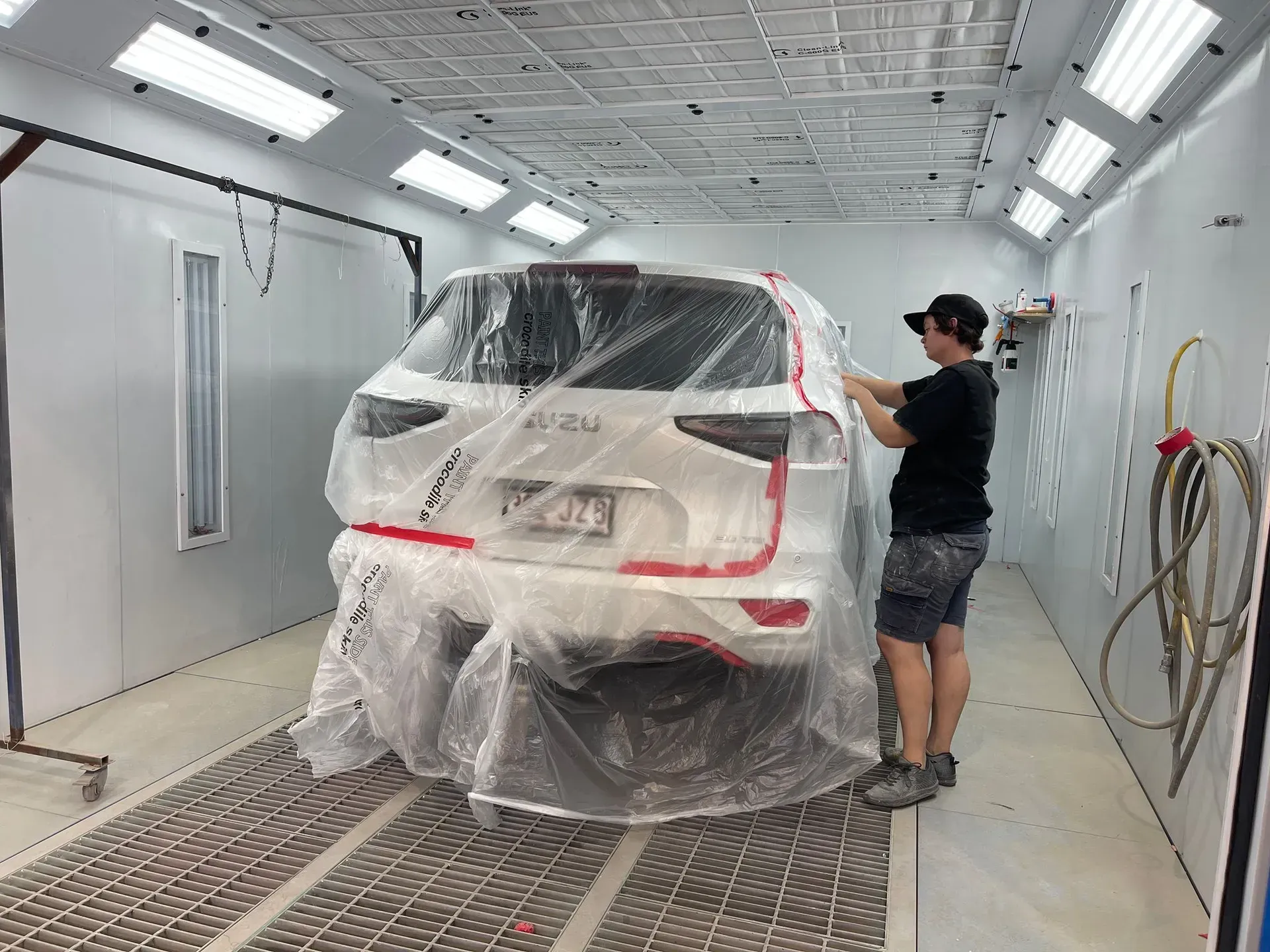 Person taping a white SUV covered in plastic in a paint booth. — Coolum Smash Repairs in Coolum Beach, QLD