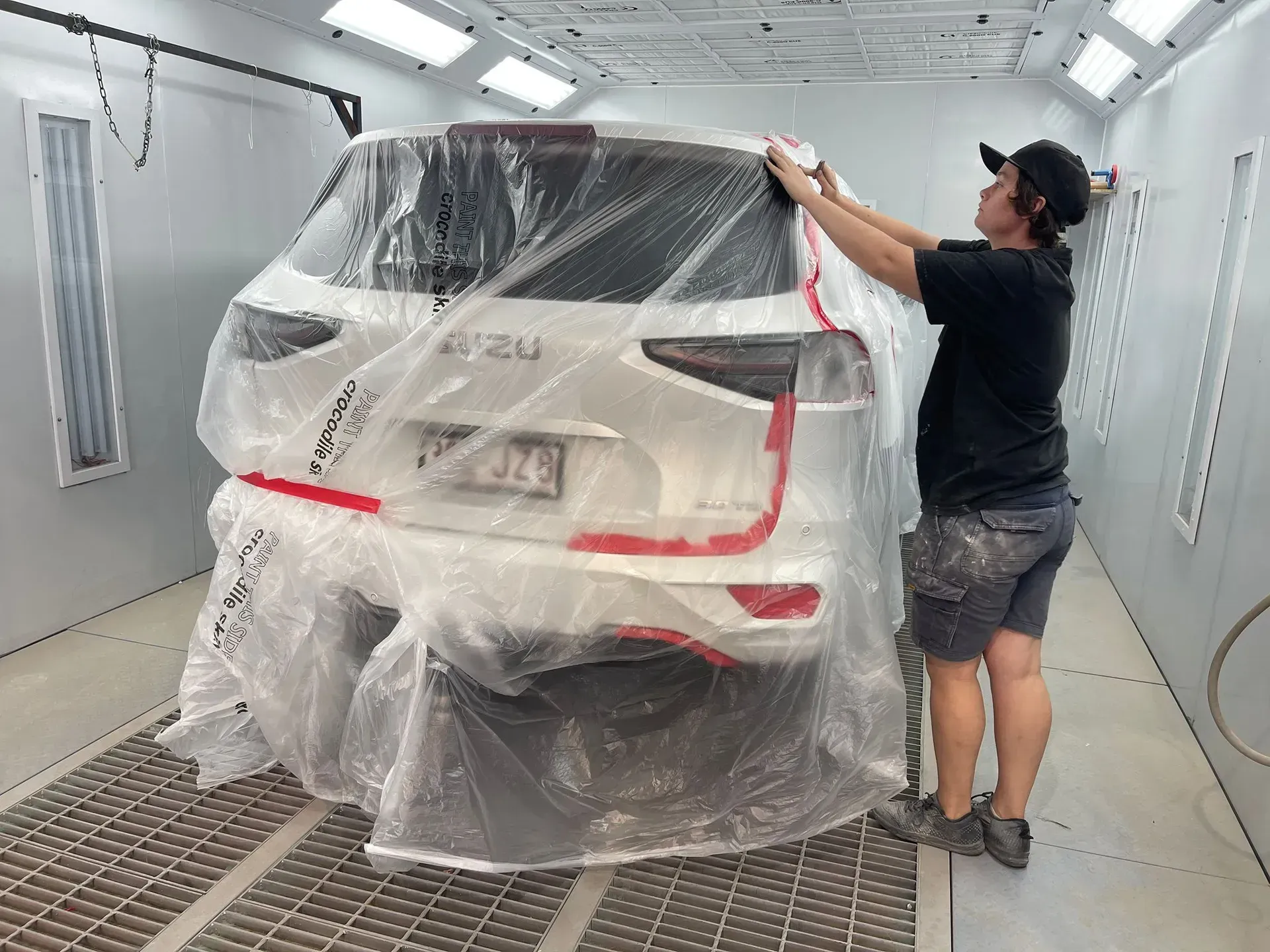 Person covering a white car in a paint booth with plastic sheeting. — Coolum Smash Repairs in Coolum Beach, QLD