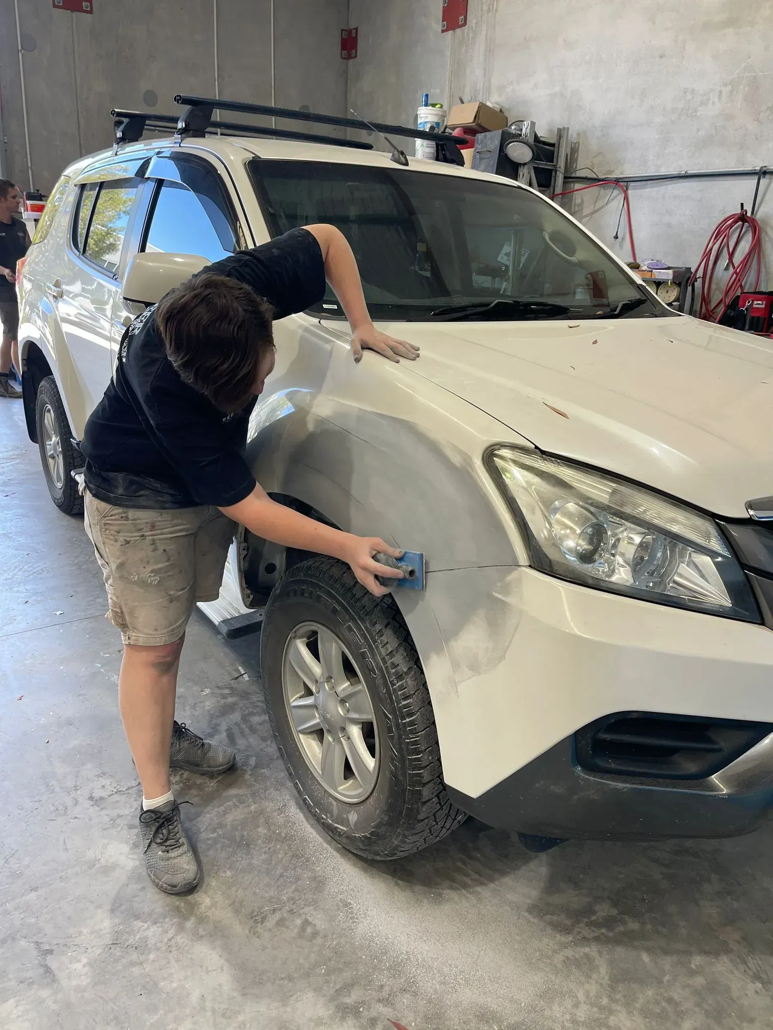 Person sanding the front fender of a white SUV in a garage. — Coolum Smash Repairs in Coolum Beach, QLD