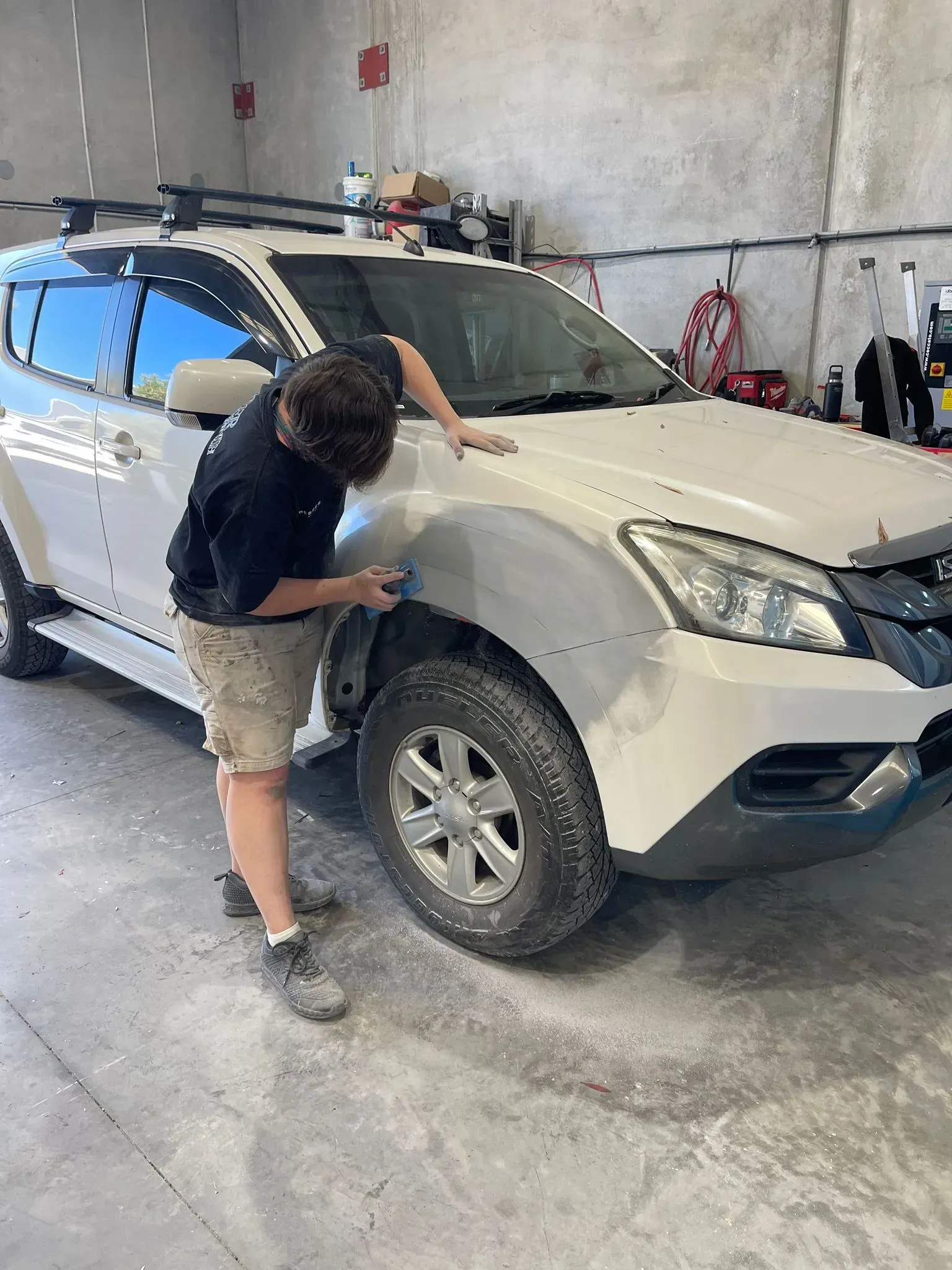 Person sanding a white car's front fender in a garage. — Coolum Smash Repairs in Coolum Beach, QLD
