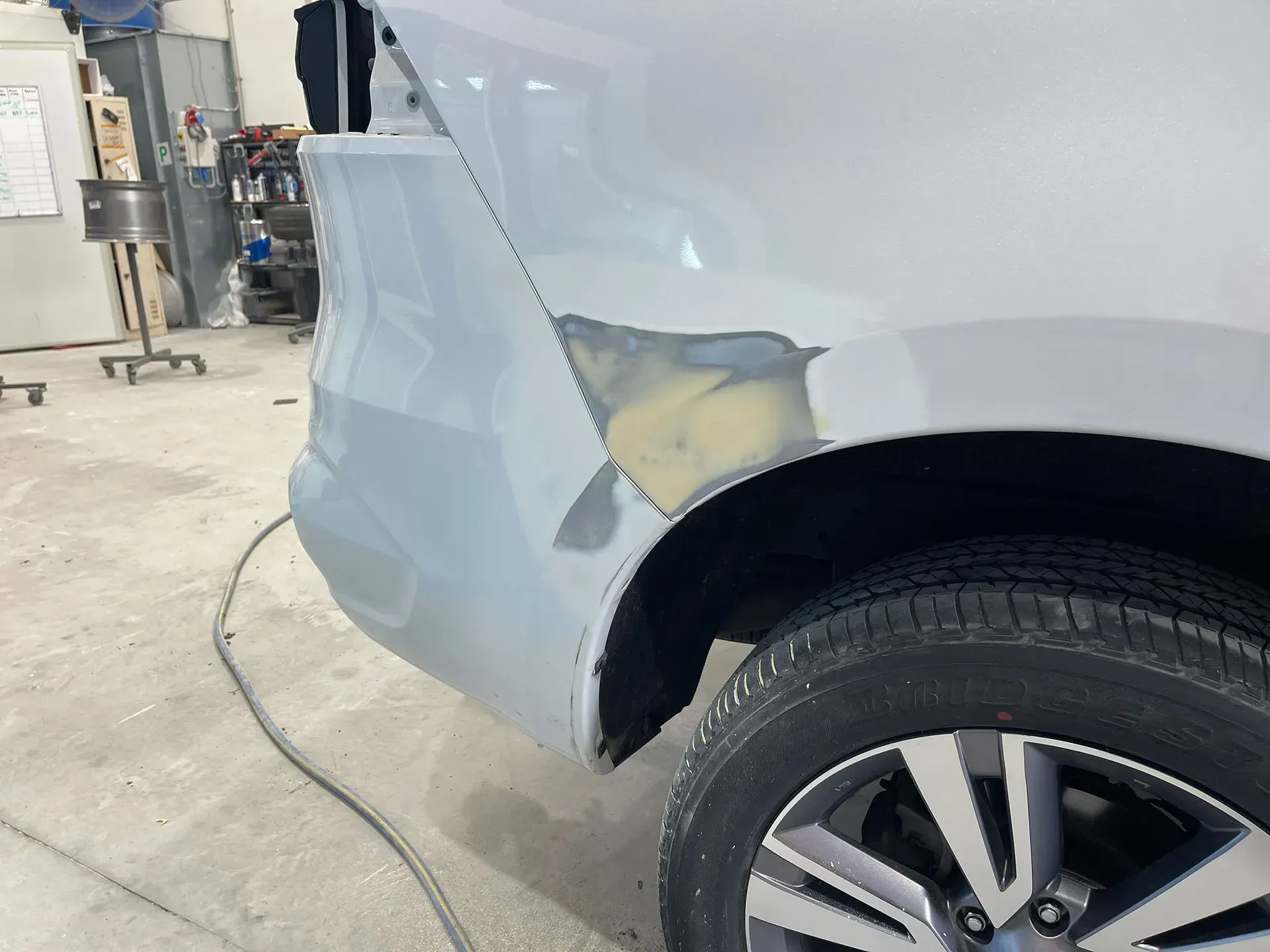 Car's rear quarter panel being repaired in a garage. Panel has body filler and is primed in gray. Tire visible. — Coolum Smash Repairs in Coolum Beach, QLD