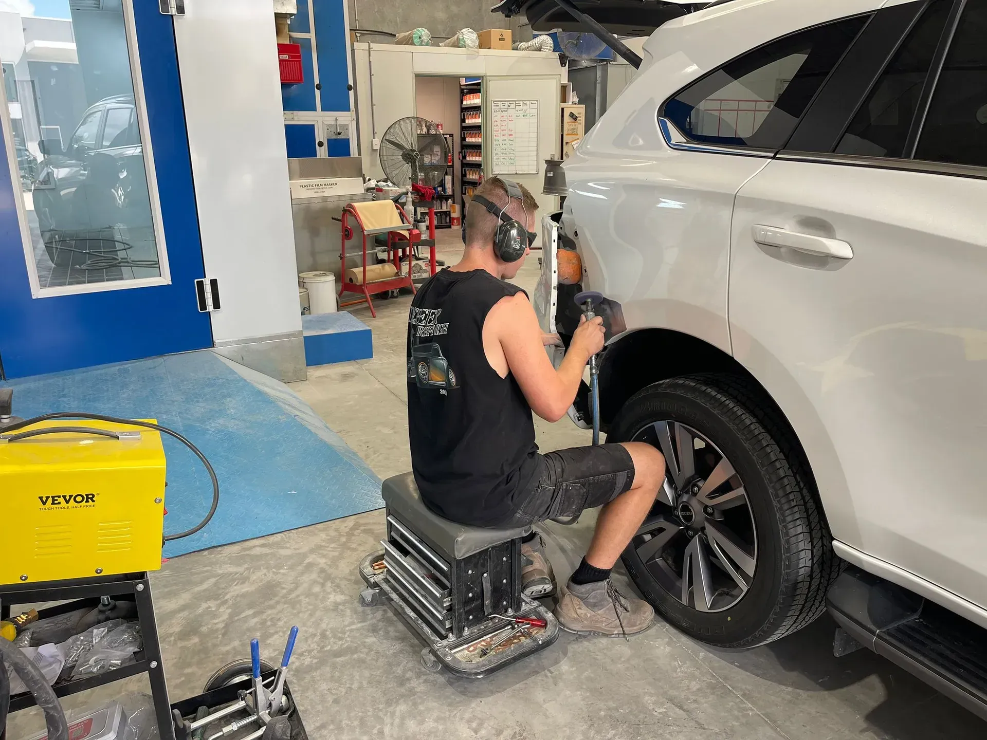 Man using a tool to repair a car's side panel in a shop.  — Coolum Smash Repairs in Coolum Beach, QLD