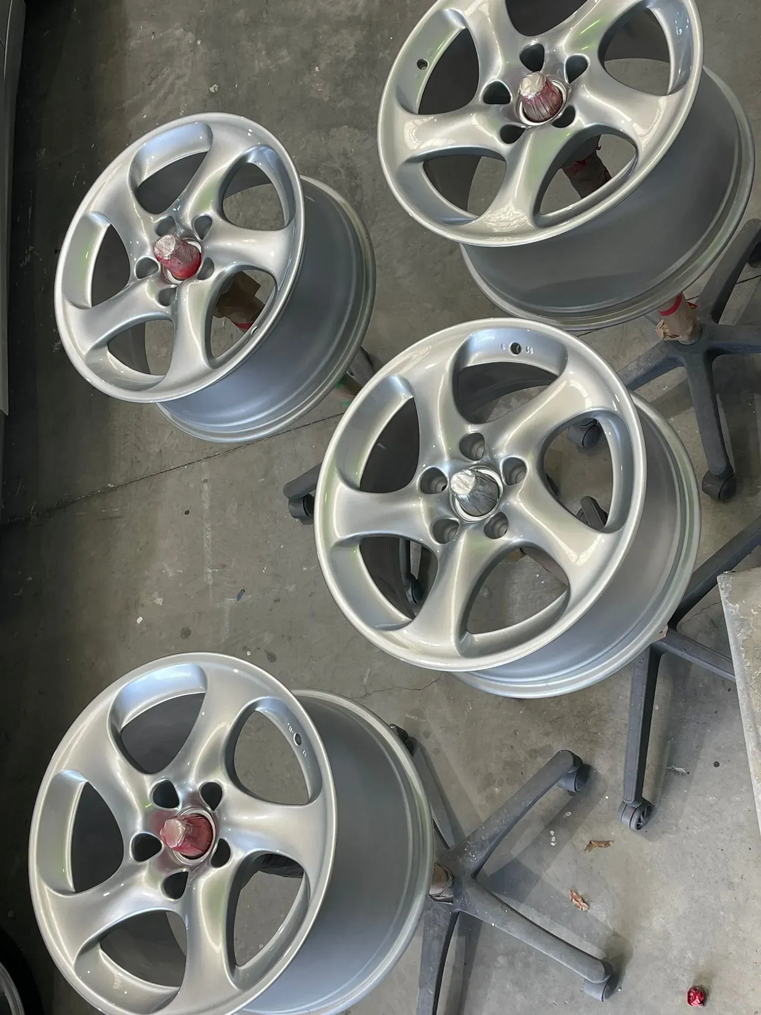 Five silver car wheels with red center caps on a gray surface, possibly a workshop. — Coolum Smash Repairs in Coolum Beach, QLD