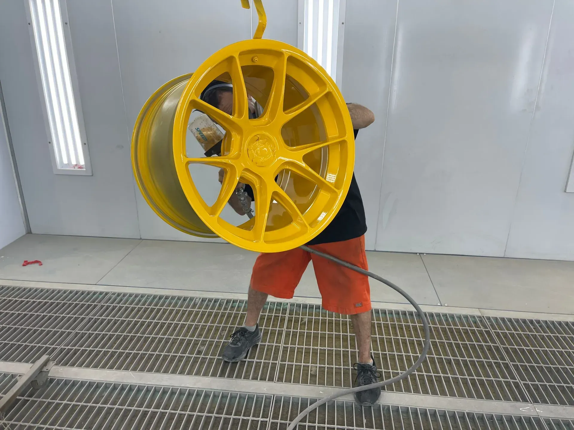 Person spraying bright yellow paint on a car wheel in a paint booth. — Coolum Smash Repairs in Coolum Beach, QLD