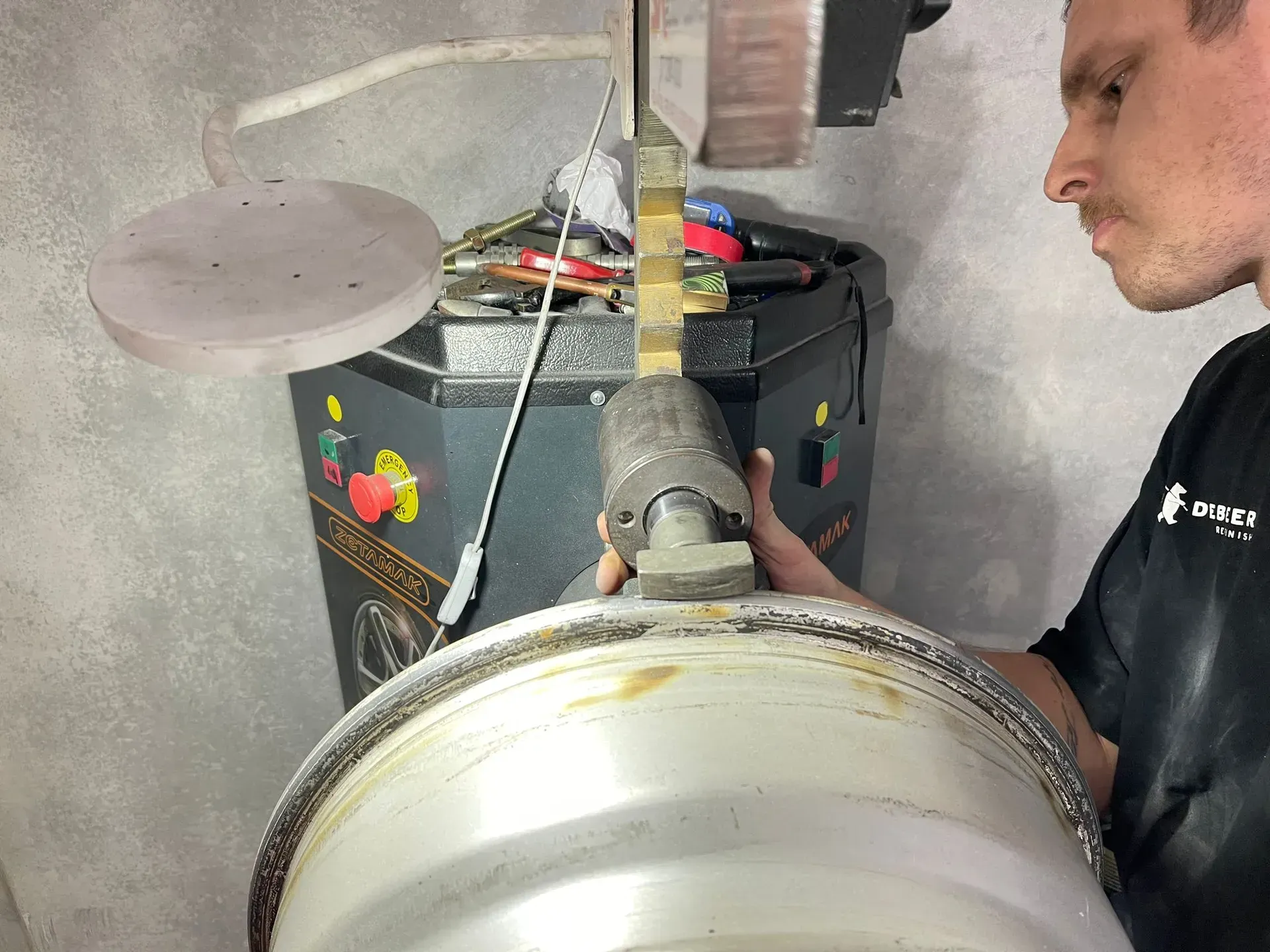 Man balancing a tire on a machine. A gray wheel sits in front of the man. The machine is black and yellow. — Coolum Smash Repairs in Coolum Beach, QLD